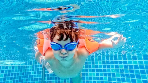Kind met zwembril en zwembandjes zwemt onder water
