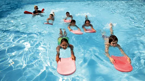 Groep kinderen oefent met zwemplankjes in het zwembad, met een lesgever op de achtergrond